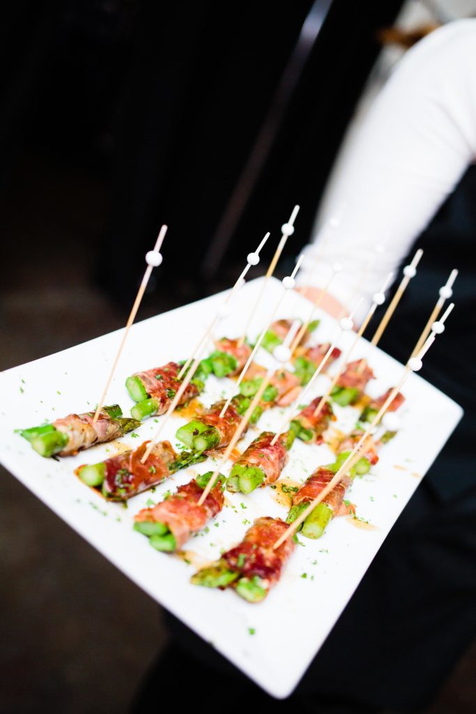 Server holding a platter of asparagus tapas with cocktail picks.