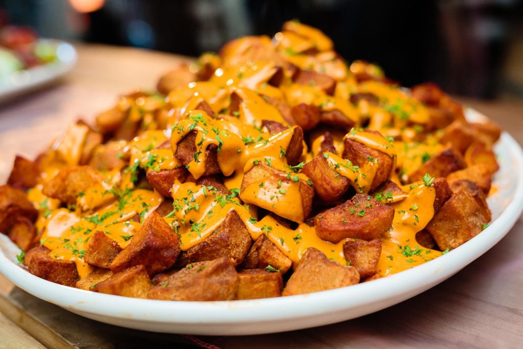 Golden potato pieces topped with bravas sauce and chopped herbs.
