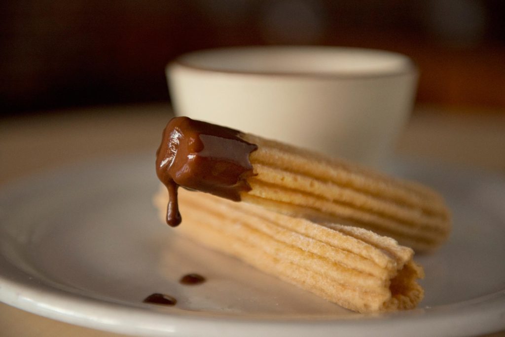 Chocolate-dipped churros beside a white cup.