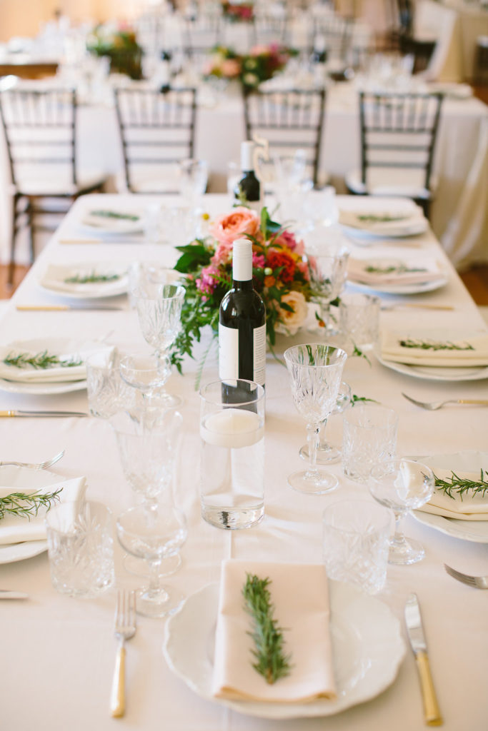 Wedding reception place settings White plates, glassware and small floral arrangements along a reception table.