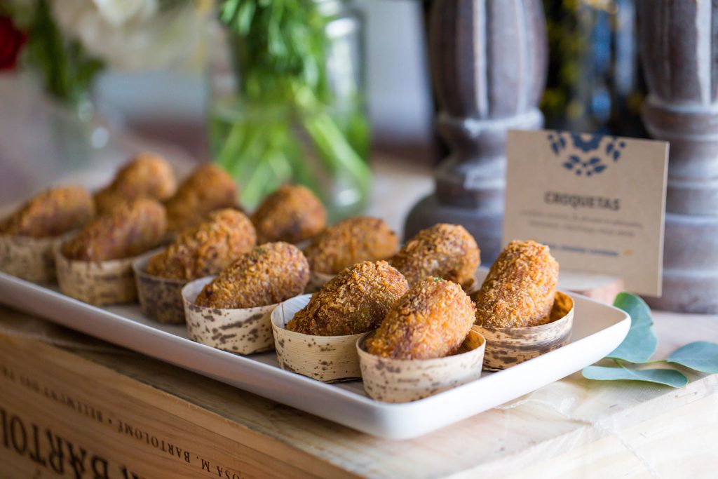 Golden croquetas in individual serving cups arranged on a white platter.