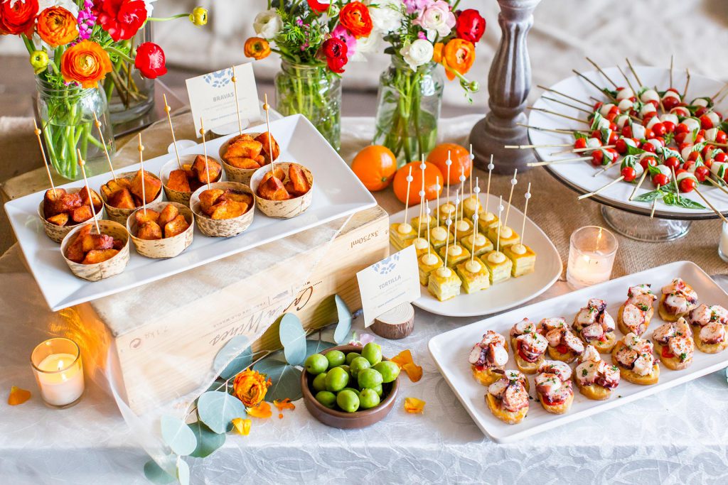 Tapas, croquetas and tortilla displayed with flowers and candles on a buffet table.