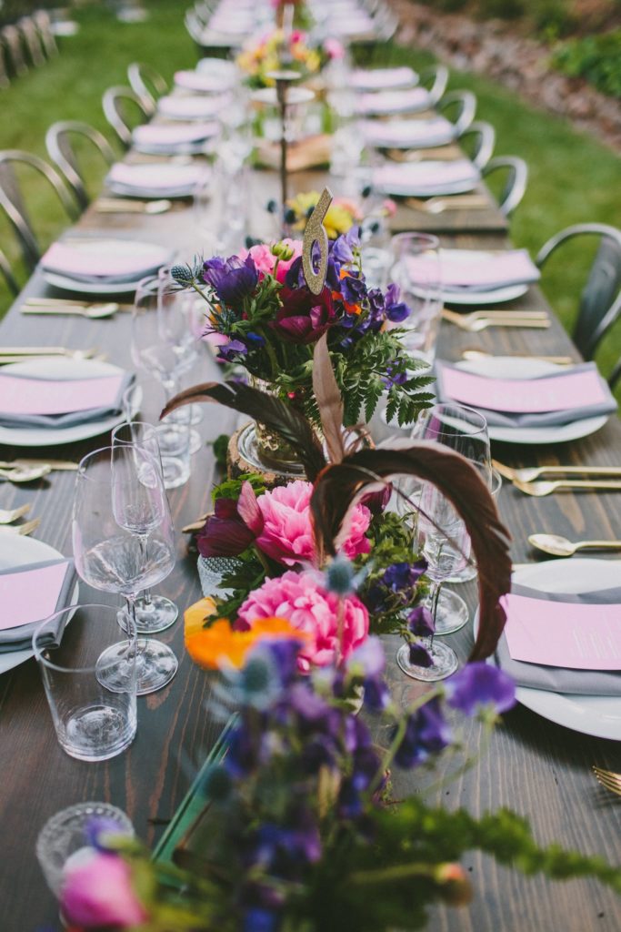 Outdoor reception table set with flowers, glassware and place settings.