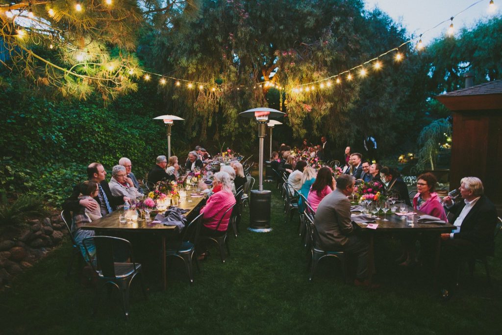 Guests enjoying dinner in a garden beneath glowing string lights.