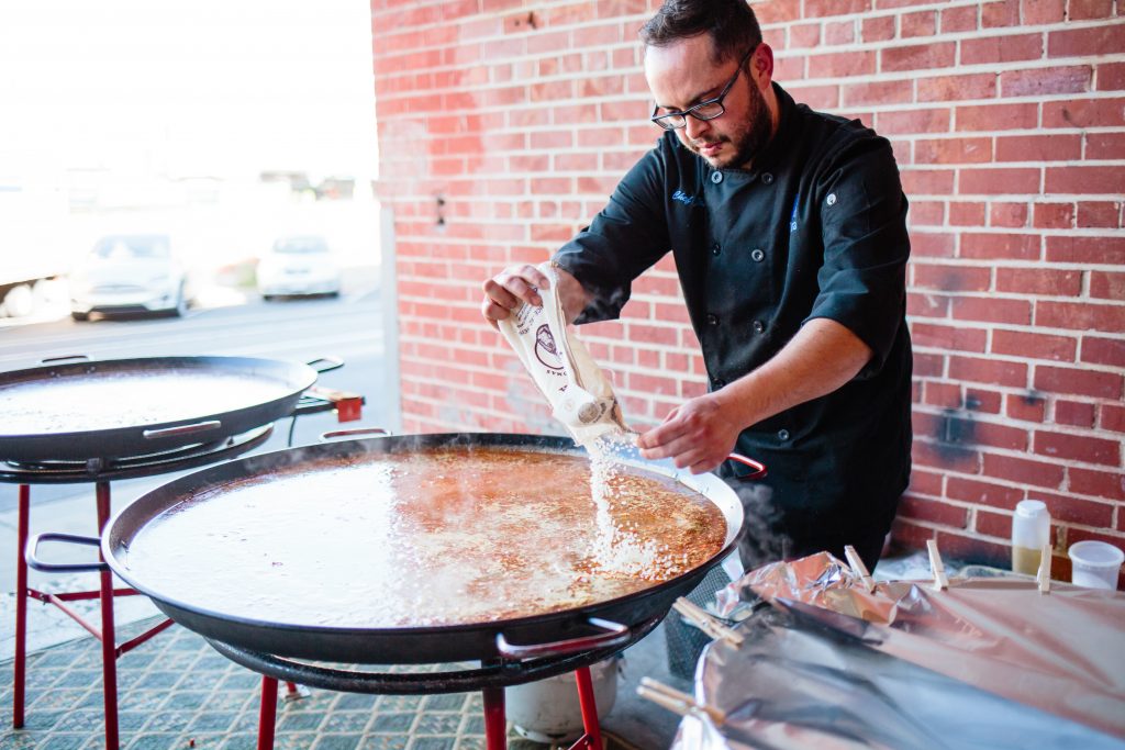Ñora chef adding rice to a large paella pan at a wedding cooking station.