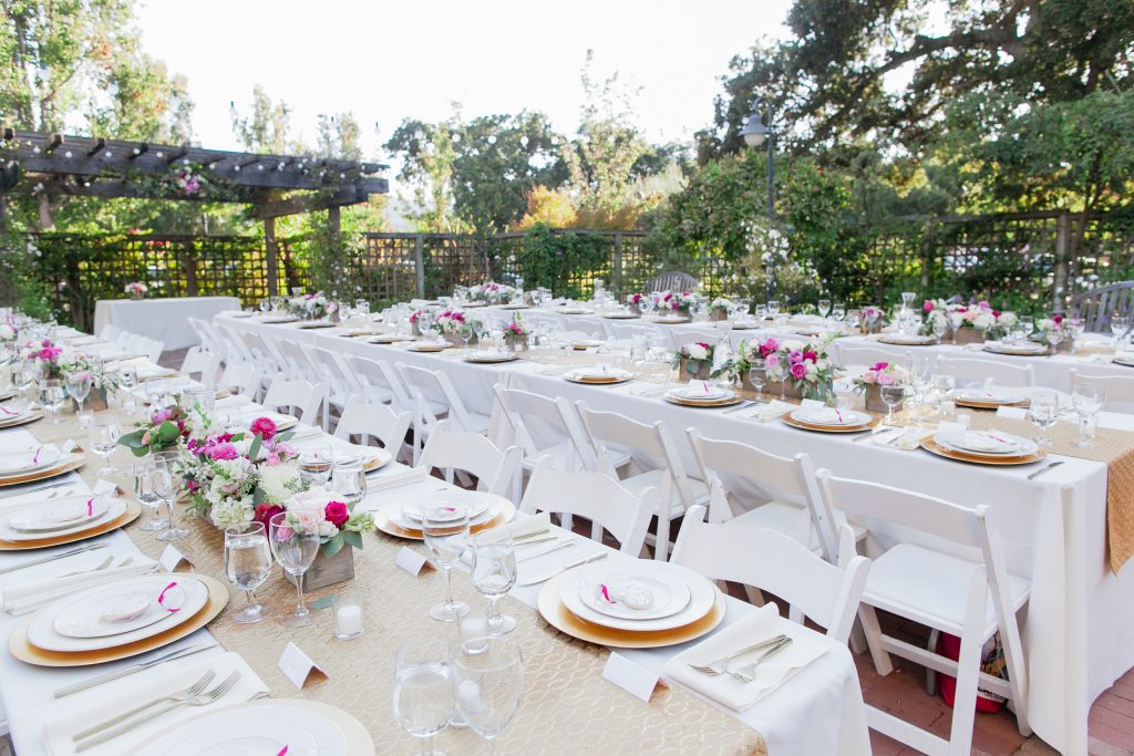 Long garden reception tables set with white chairs, flowers and glassware.
