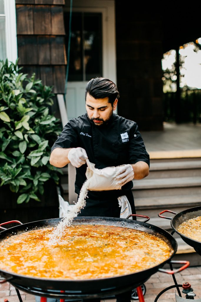 Chef adding rice to a paella pan A chef adding rice to a large paella pan at an outdoor event.