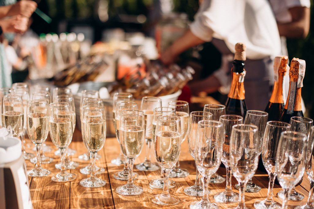 Wine glasses, champagne flutes and bottles lined up on a wooden bar table.
